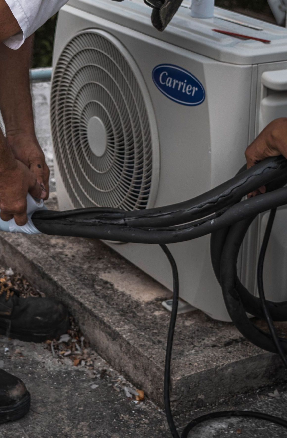 A technician performs maintenance on an outdoor air conditioning unit, focusing on hose connections.