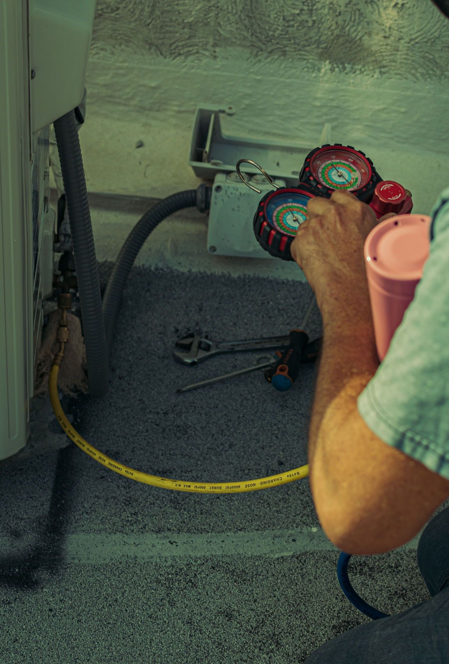 A technician checks and repairs an HVAC system outdoors using tools and gauges.